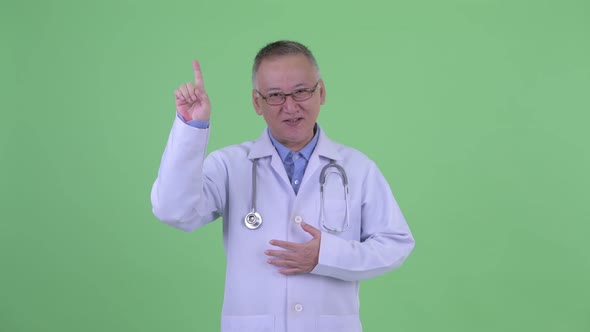 Happy Mature Japanese Man Doctor Talking While Pointing Up