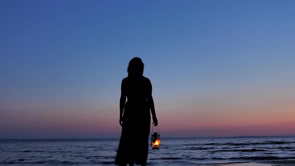 Lonely Female in Dress with Kerosene Lantern Looking at Sunset Sky at Night