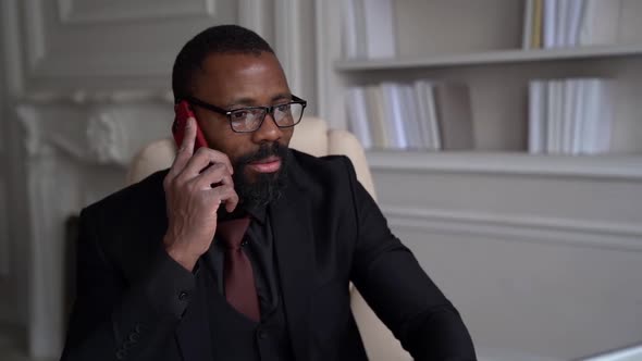 African-American Bearded Man in a Black Suit, Shirt, Stylish Glasses. A Businessman Works on a