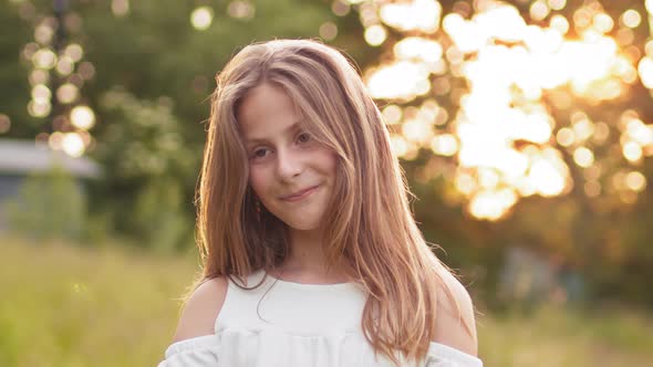 Attractive Young Blonde Teen Girl Walking in Summer Sunset Park Looks at Camera