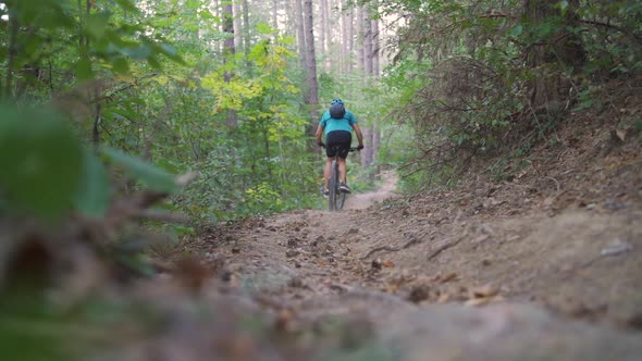 Young Mountain Biker Climbs on a Path in a Forest