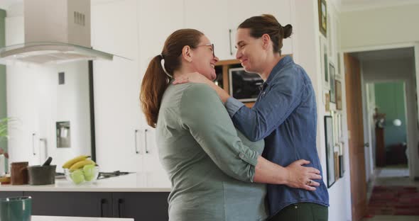 Caucasian lesbian couple smiling and dancing in kitchen