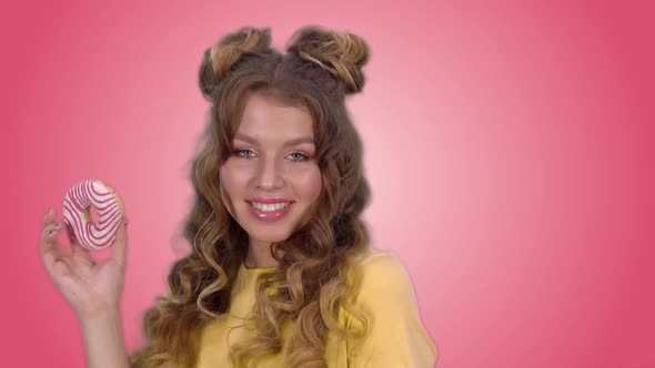 Attractive Girl in a Yellow Shirt Posing with a Donut Winks and Smiling While Looking at the Camera