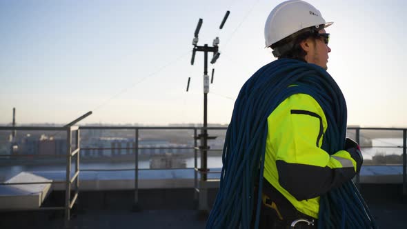 Climber with Skein of Rope on Shoulder Walks Along Rooftop