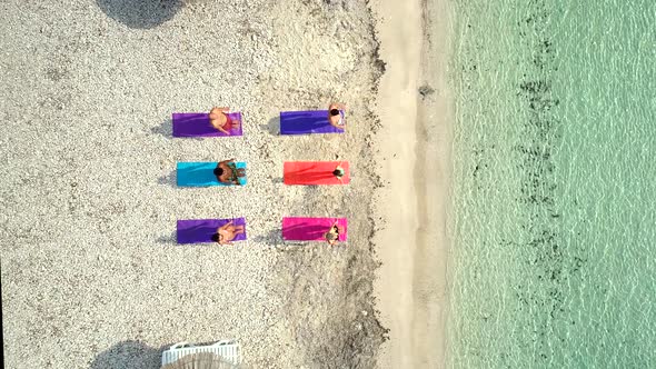Aerial view of group of people doing yoga on colourful mats on the beach.