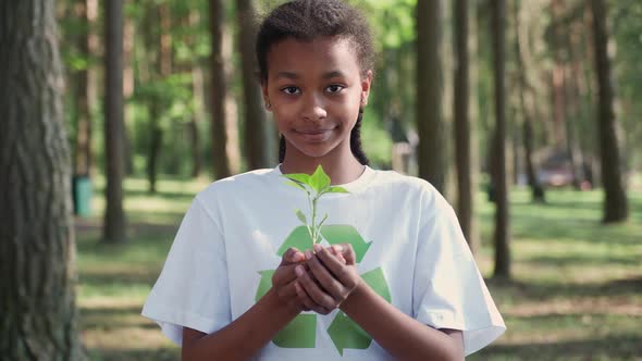 Young African Female Volunteer Holds a Small Flower Plant in Her Hands and Looks at the Camera a