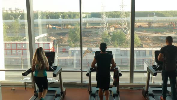 Three Sports People Two Men and Woman Running on Treadmills in a Gym
