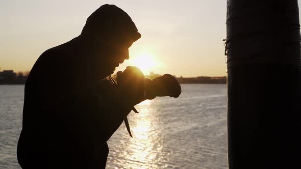 Boxer training on sunset background. Silhouette. Beats a punching bag. Martial arts. Slow motion