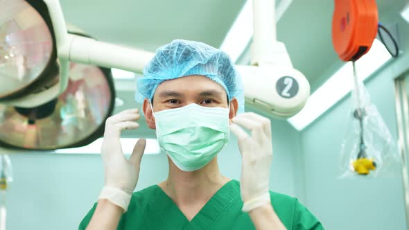 Portrait of Asian surgeon with medical mask standing in operation theater at a hospital. Team of Pro