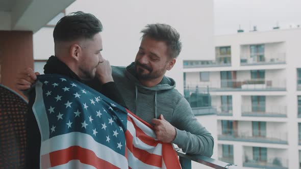 Happy Handsome Gay Couple Hugging Under USA Flag on the Balcony