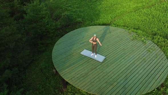 The girl does aerobics outdoors in the field on the mat. Aerial view