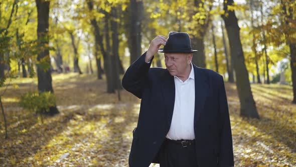 Thoughtful Senior Man in a Suit Corrects Hat and Looks Aside in Park