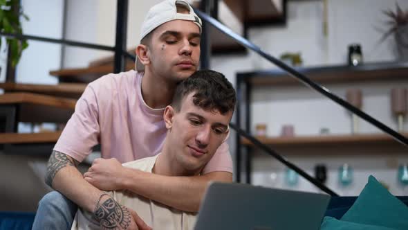 Portrait of Relaxed Young Gay Man Surfing Social Media on Laptop Talking with Boyfriend Smiling