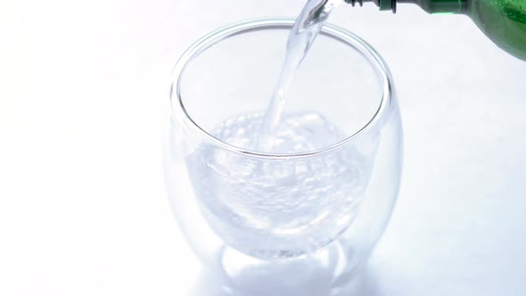 woman is pouring mineral water from green color plastic bottle in double wall insulated glass