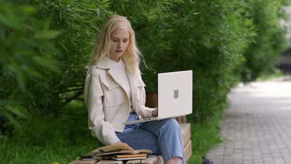 Woman Student with Laptop and Books Sits on a Park Bench