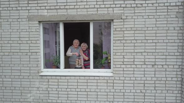 Old Grandparents Couple Cooking Barbecue on Electric Grill on Windowsill at Home