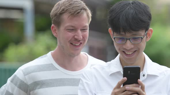 Two Happy Multi-ethnic Businessmen Using Phone Together in the Streets Outdoors