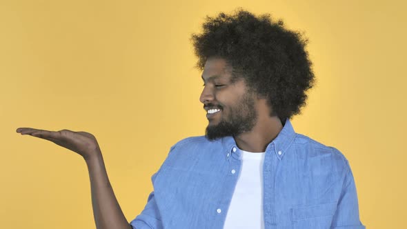 AfroAmerican Man Showing Product at Side Yellow Background