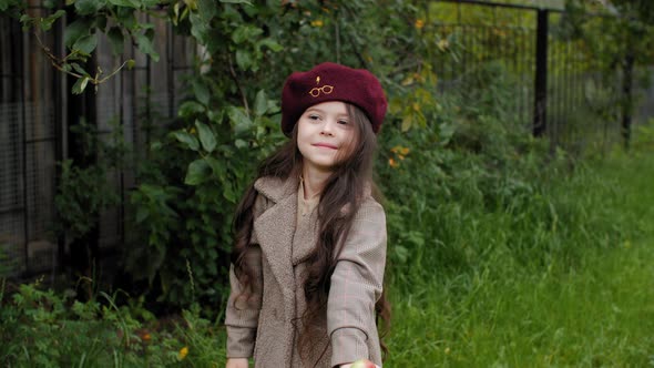 Joyful Teenager Girl in Coat and Beret Holding Ripe Apple in Hand at Fruit Garden. Happy Young Girl