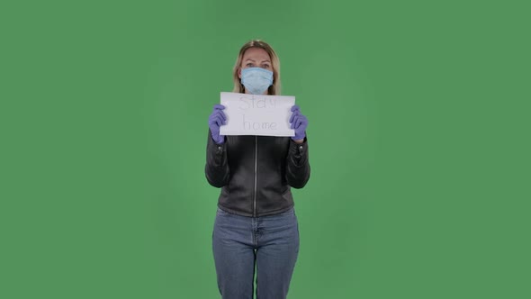 Portrait of Beautiful Young Woman in Medical Mask Is Looking at Camera and Holding a Poster 