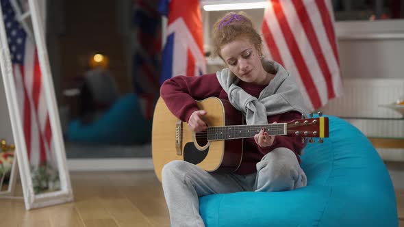 Wide Shot Portrait of Concentrated Caucasian Female Musician Playing Guitar Singing Sitting on