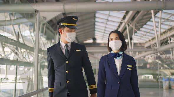 Airliner pilot and air hostess wearing face mask, walking in airport terminal to the airplane.