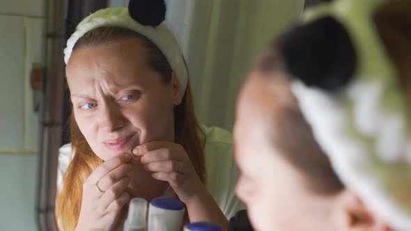 Young Woman Looks at Herself in the Bathroom Mirror Examines the Skin of Her Face Finds Pimple and