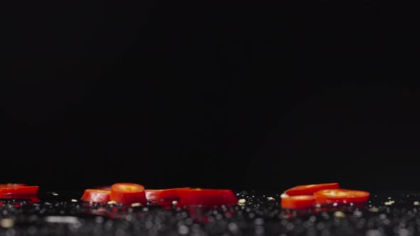 Slices of Red Hot Chili Pepper Falling on Wet Surface on Black Studio Background