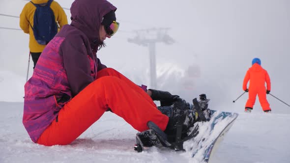 Girl with Snowboard Sitting on Top and Enjoying Mountain Landscape. Sport Woman in Snowy Mountains