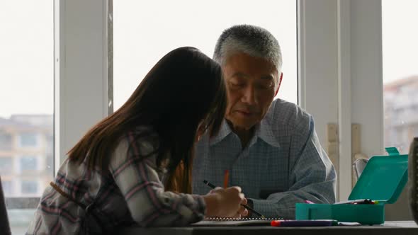 Old senior asian grandfather helping his granddaughter with homework in a comfortable home 4k