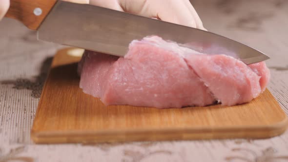 Metal Knife Cuts Up the Meat. Cutting Meat on a Wooden Board. Pork Is on the Board. Sliced Pork Meat