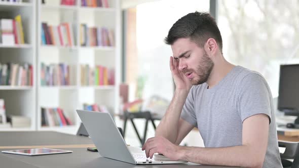 Young Man with Headache Using Laptop in Office