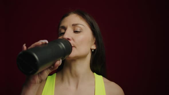 Athletic Young Woman Drinking Water From a Bottle on a Dark Background