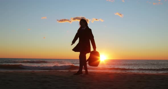 Silhouette of Young Girl with Backpack Cheerfully Dances at Sunrise on the Beach