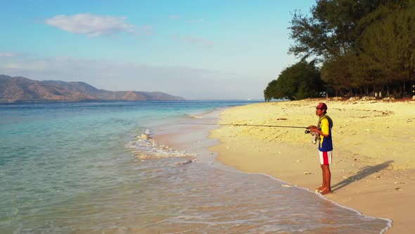 Guy fishing on tropical lagoon beach break by blue ocean with white sandy background of Gili Meno in