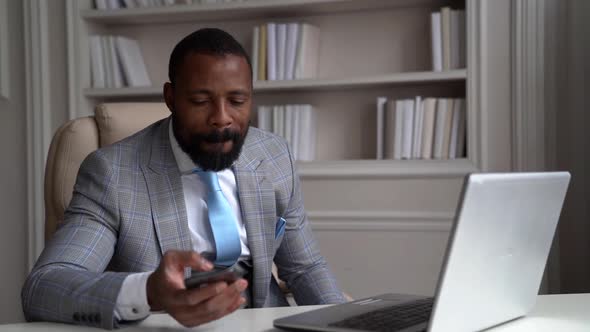 African-American Bearded Man in a Gray Suit, White Shirt. The Businessman Is on the Desktop at a