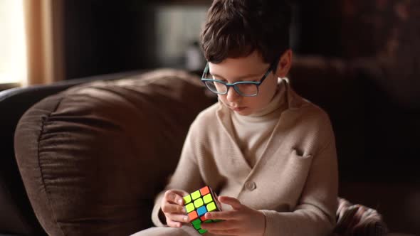 Medium Shot of Smart Child Boy Wearing Eyeglasses Solving Rubik Cube and Talkign at Home