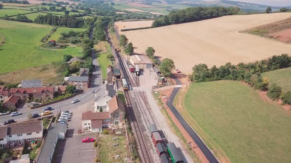 Drone shot tracking forward over a village and train station, with a Diesel engine at the station. S