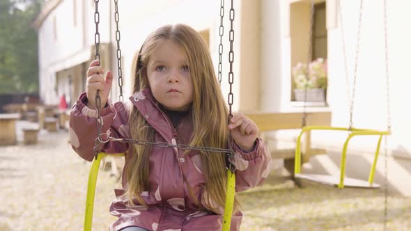 Cute Little Caucasian Girl Looks Bored As She Sits on a Swing Ride in a Restaurant Garden