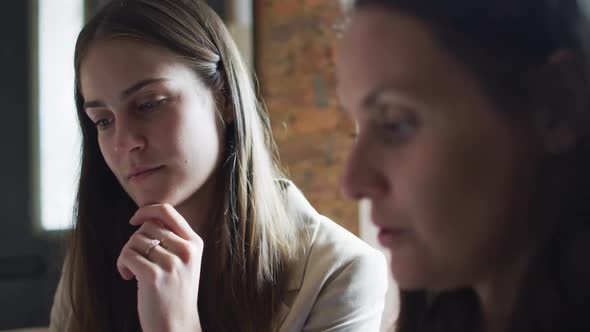 Portrait of two caucasian businesswomen sitting at table, talking, having business meeting