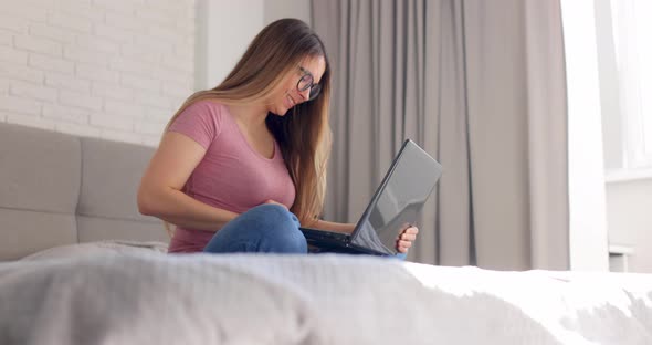 Woman with Glasses Working and Closes Laptop Sitting on the Bed Bed at Home on Morning