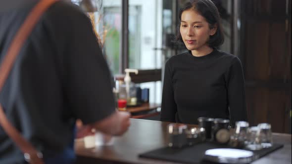 4K Asian man barista preparing takeaway order hot coffee to customer on bar counter.