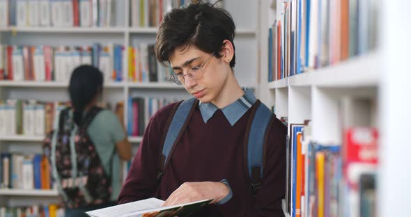 Student Reading Book in Library Leaning on Bookshelf