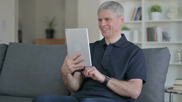 Middle Aged Businessman Celebrating Success on Tablet at Home 