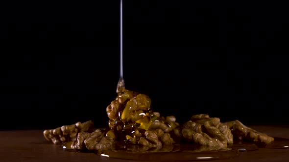 Pour Honey on Walnuts Which Lie on a Wooden Board on a Black Background