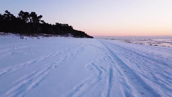 Beautiful romantic aerial shot flying over a snow covered beach after the sunset on the calm Baltic