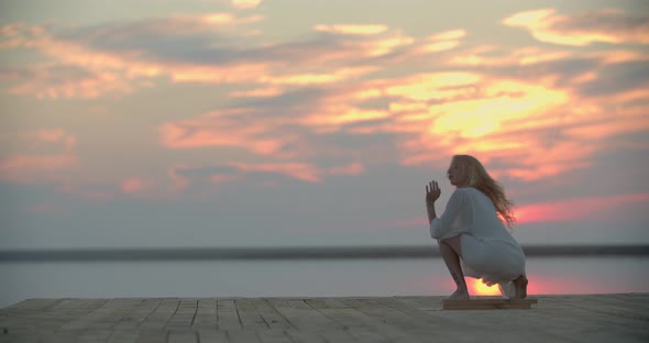 Blonde Woman is Dancing on the Wooden Pier of a Lake Reflection of the Sunset