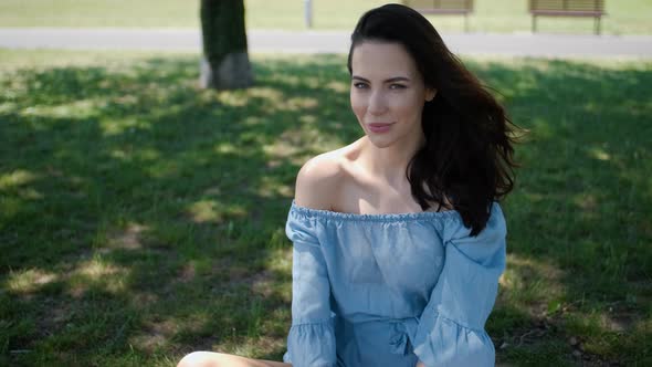 Portrait of Attractive Brunette Woman in Blue Dress Sitting in a Park