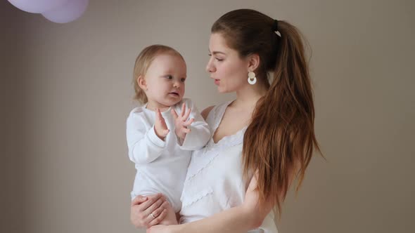 Mother in a White Coat Holds Her Little Blonde Daughter Against the Wall