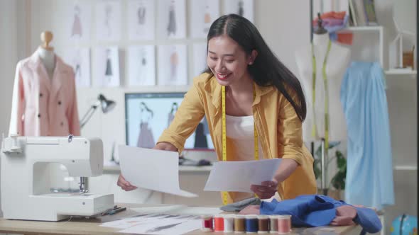 Female Designer With Sewing Machine Rearranging And Looking At The Papers While Designing Clothes